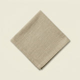 A folded beige linen napkin with a subtle horizontal textured weave, displayed on a solid cream-colored background.