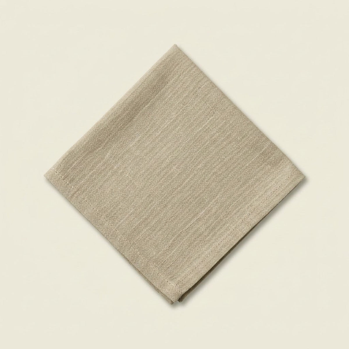 A folded beige linen napkin with a subtle horizontal textured weave, displayed on a solid cream-colored background.