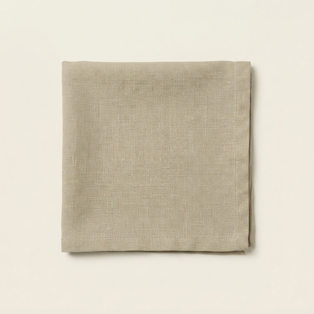 A folded square linen napkin in a light taupe-beige color, displayed flat against a matching off-white background.