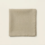 A folded square linen napkin in a light taupe-beige color, displayed flat against a matching off-white background.
