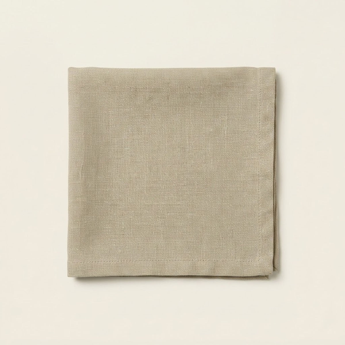 A folded square linen napkin in a light taupe-beige color, displayed flat against a matching off-white background.