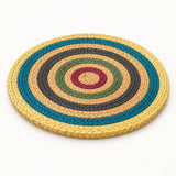 A round woven straw placemat in a natural light tan color, photographed from a top-down angle on a solid white background.