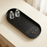 An oval black tray with rounded corners sits on a light beige table. Two small clear glass bottles are placed in the left side of the tray, and a gold necklace with two small gold pendants is laid on the right side.