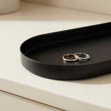 Two minimalist metal rings, one rose gold and one silver, displayed on a black oval tray set on a cream-colored surface.