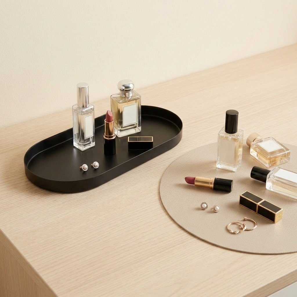 A styled tabletop arrangement featuring a black oval tray holding two perfume bottles and small accessories, alongside a round beige mat with additional cosmetics and perfume bottles on a light wood surface.