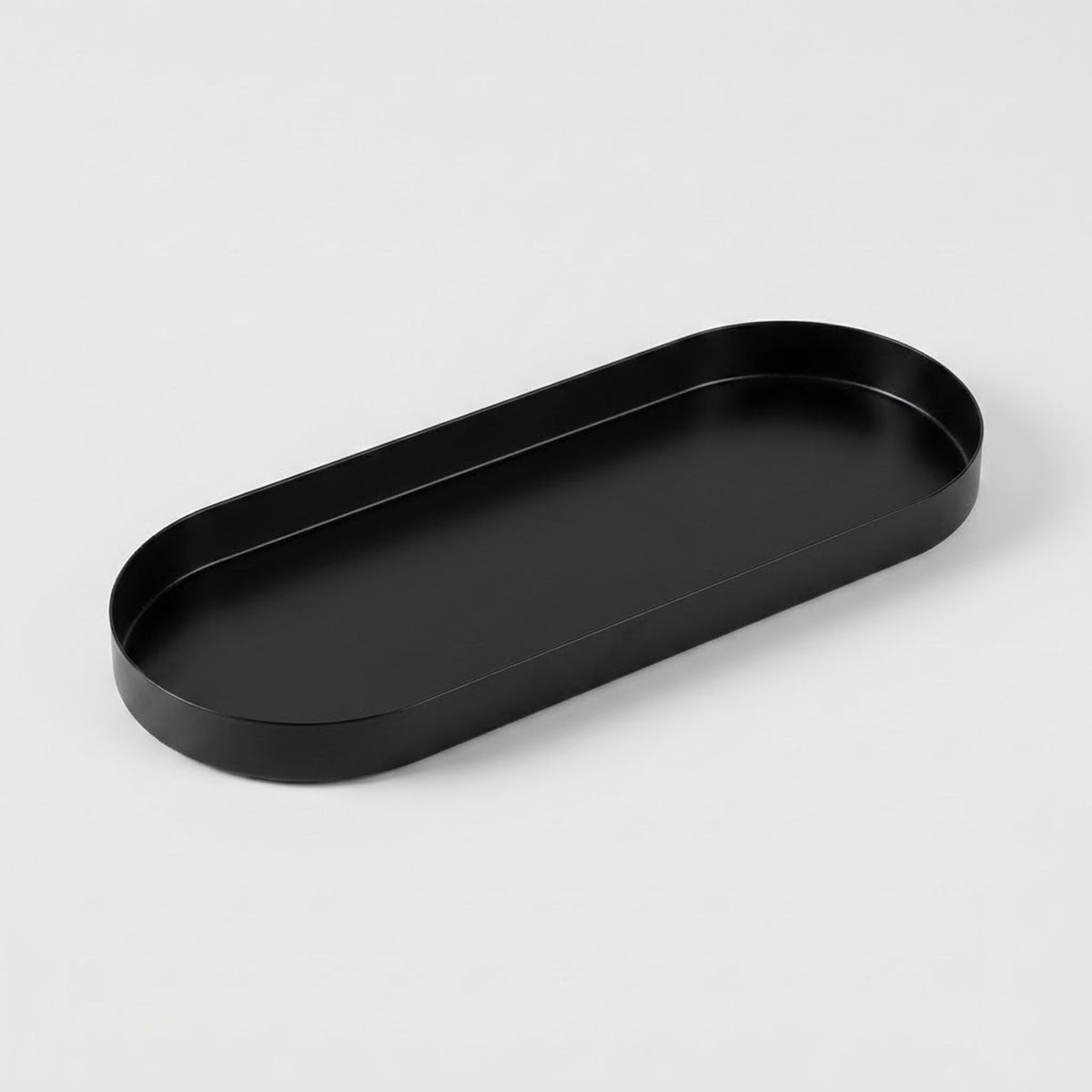 A minimalist black metal tray with a rounded rectangular shape, photographed on a clean, light gray background.