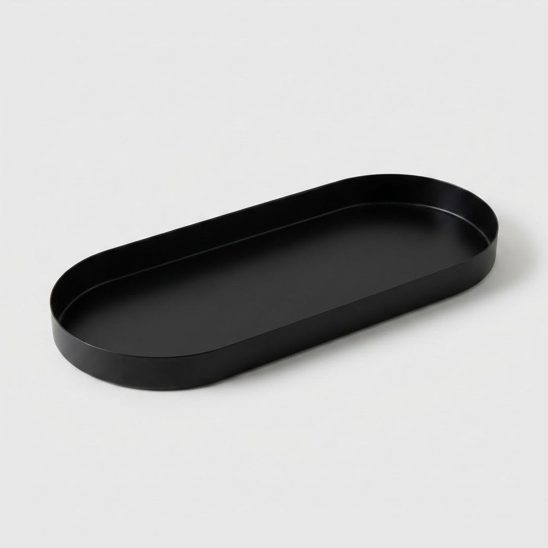 A minimalist black metal oval tray with a shallow depth, photographed on a clean, light gray background.