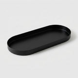 A minimalist black metal oval tray with a shallow depth, photographed on a clean, light gray background.