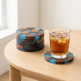 A set of round wooden coasters with a blue and brown checkerboard pattern, shown on a light wood table. One coaster holds a glass of iced coffee with ice, while a stack of coasters sits beside it.
