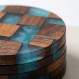 A close-up of a stack of round coasters with a geometric wood and translucent aqua resin pattern, set against a clean white background.