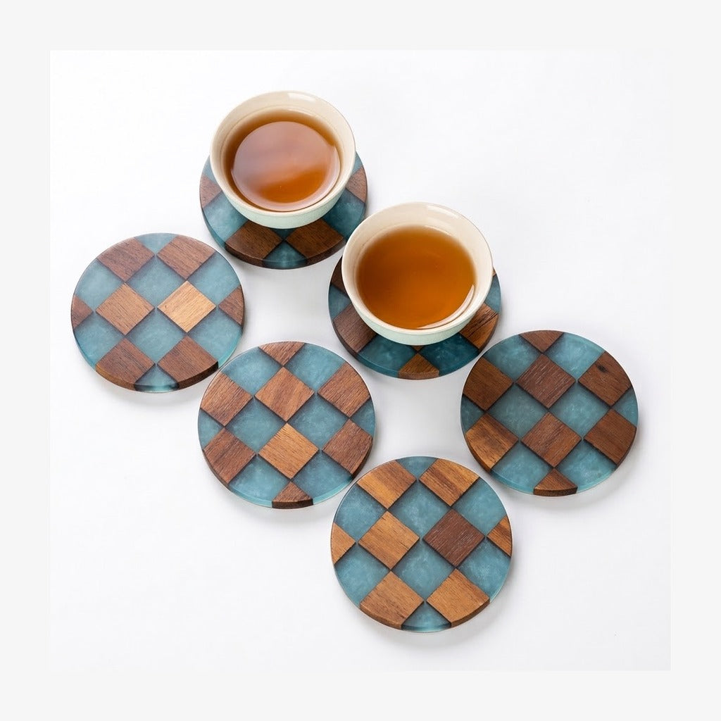 Six round wooden coasters with a blue and brown checkerboard pattern, arranged on a white background. Two coasters are holding white ceramic cups filled with tea.