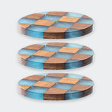 Three round wooden coasters with a blue and brown checkerboard pattern, shown on a light gray background.