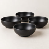 Four black Japanese-style bowls display their smooth rounded shape in a clean tabletop arrangement.