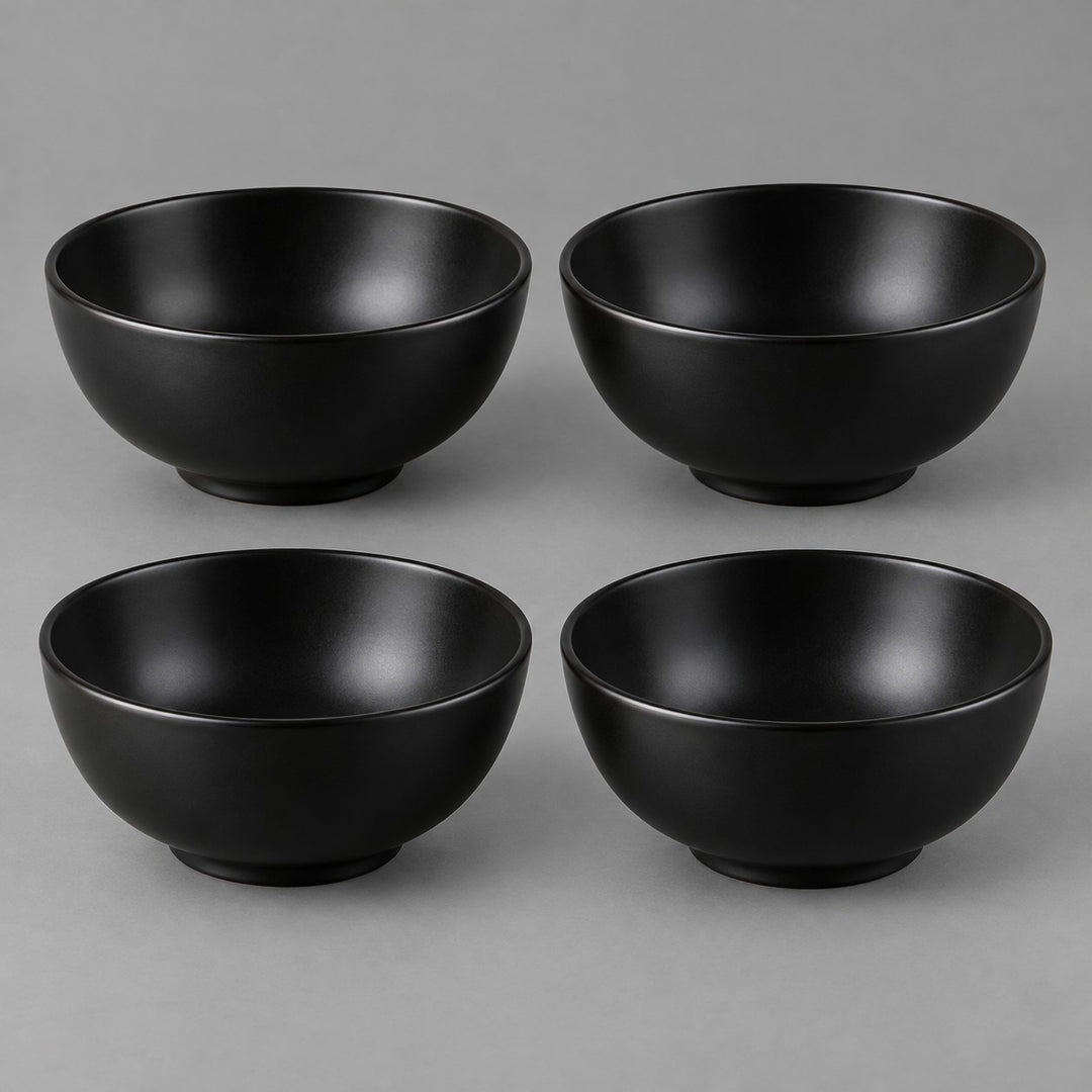 Four black Japanese-style bowls are centered together against a soft charcoal studio backdrop.