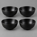 Four black Japanese-style bowls are centered together against a soft charcoal studio backdrop.