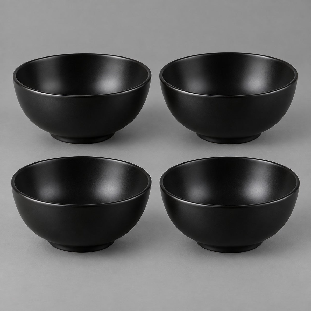 Four black Japanese-style bowls are centered together against a soft charcoal studio backdrop.