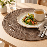 Brown woven polyester placemat catches a small spill beneath tableware on a wooden dining table.
