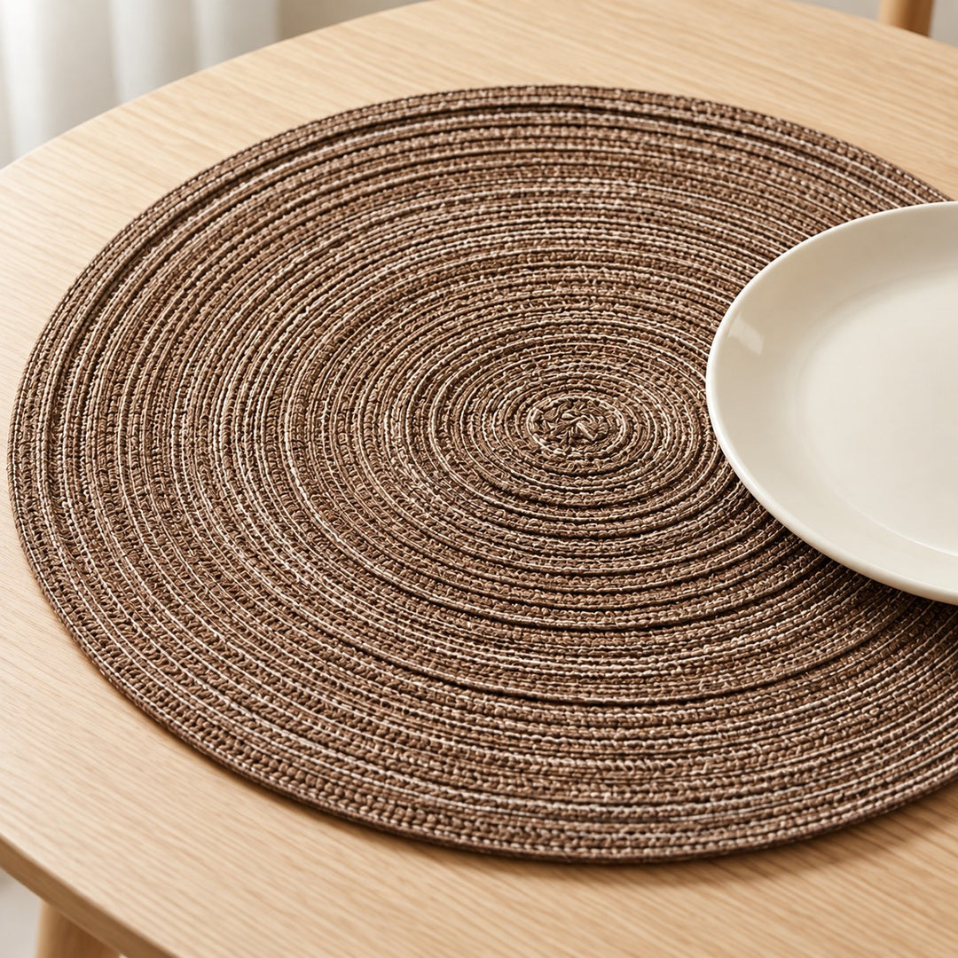 Brown round placemat shows its thick concentric braid beneath a simple ceramic plate on an oak table.