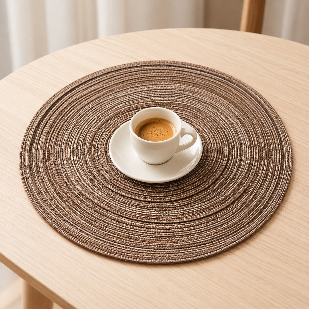 A small espresso cup and saucer sit on the compact brown woven placemat on a wooden table for scale.