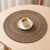 A small espresso cup and saucer sit on the compact brown woven placemat on a wooden table for scale.