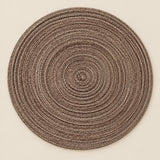 Single brown round woven polyester placemat centered on a softly tinted warm beige studio background.