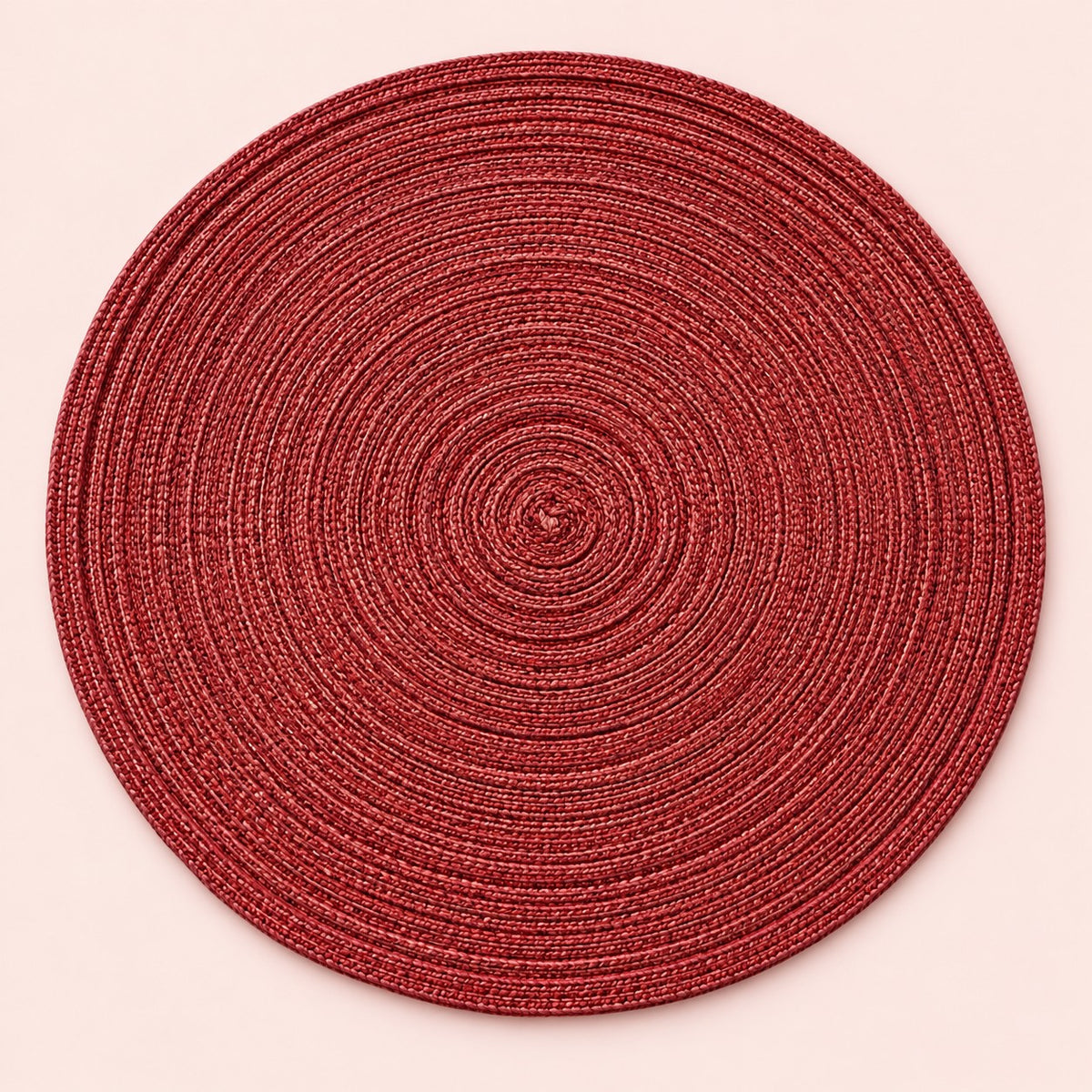 Single red round woven polyester placemat centered on a softly tinted blush studio background.
