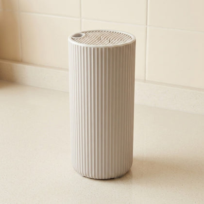 A ribbed cylindrical white container or dispenser standing on a light countertop against a tiled wall.