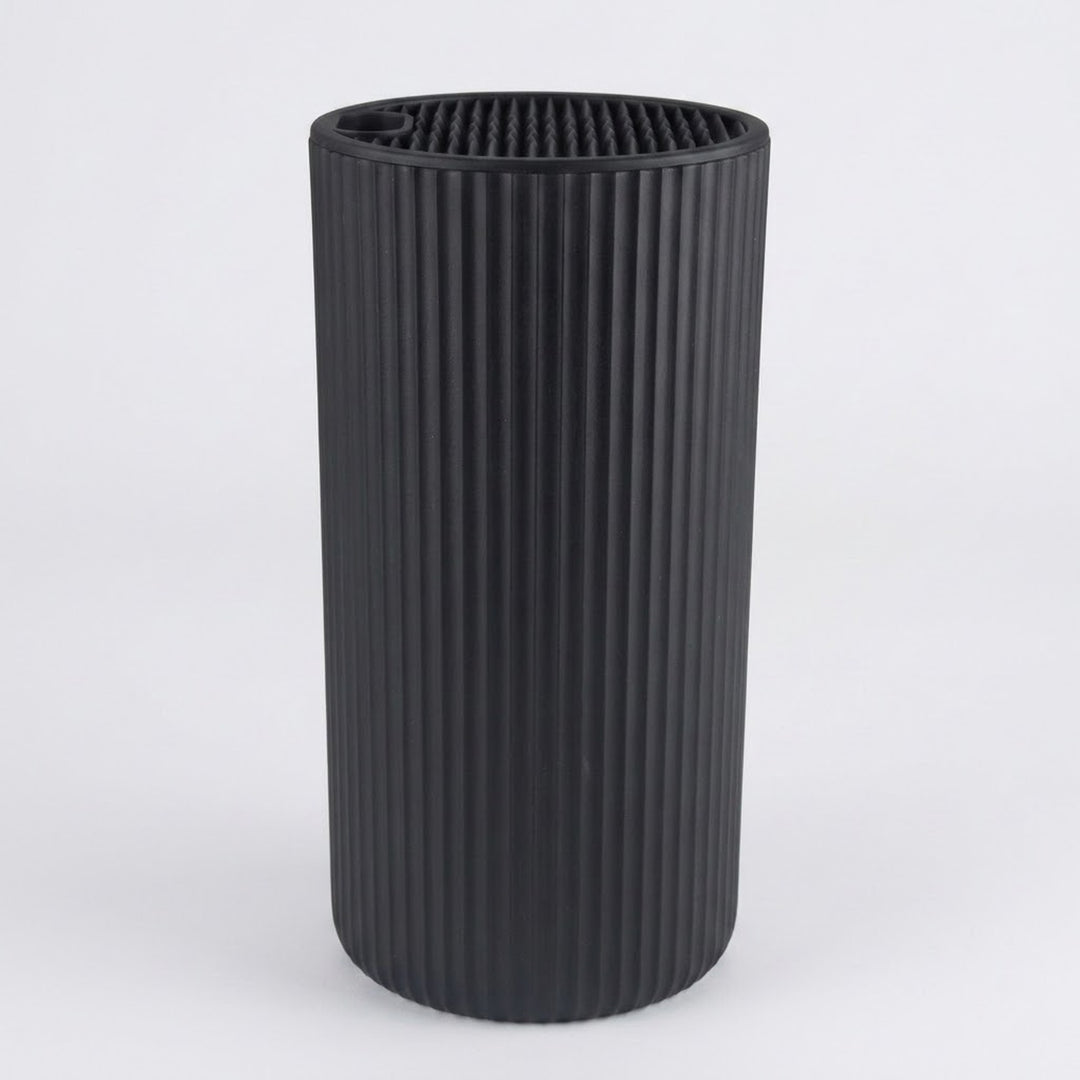 A black ribbed cylindrical container or vase with a fluted vertical texture, shown on a light gray background.