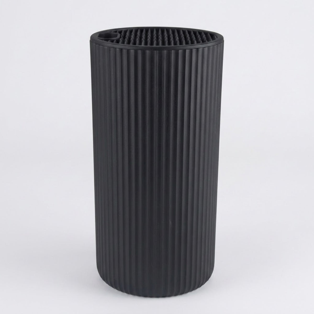 A black ribbed cylindrical container or vase with a fluted vertical texture, shown on a light gray background.