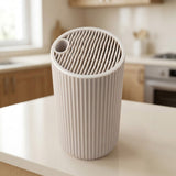 A ribbed cylindrical air purifier in a light beige color, shown on a kitchen countertop with a blurred kitchen background.