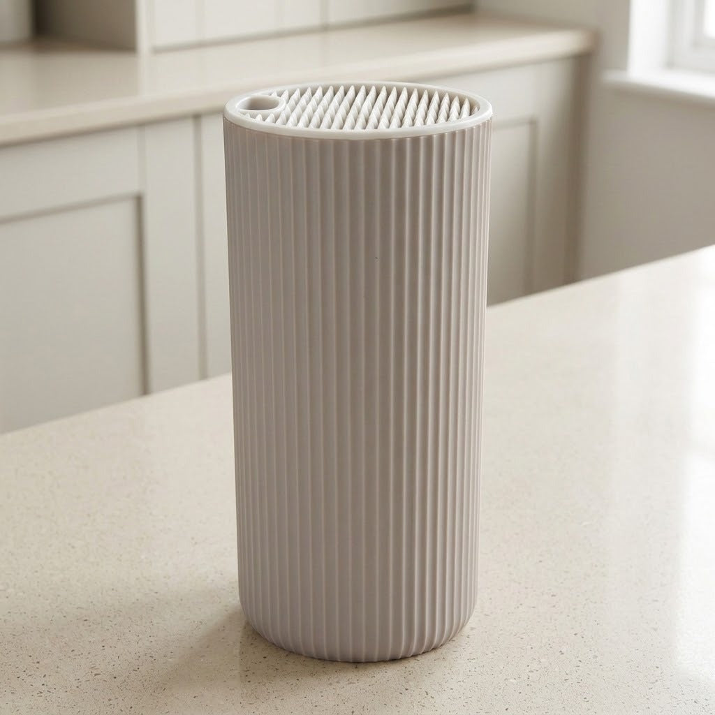 A ribbed cylindrical container or planter in a light warm gray or off-white color, standing on a speckled beige countertop with a blurred kitchen background.