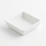 A small square white ceramic dish with a shallow interior, photographed on a clean white background.