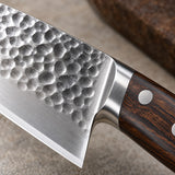 A close-up of the 15-piece hammered kitchen knife set shows a dimpled stainless blade and Pakka wood handle.