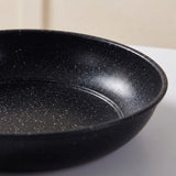 A close-up of a black non-stick frying pan with white speckles, showing the interior surface and rim on a light-colored surface.