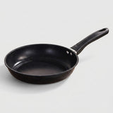 A black non-stick frying pan with a textured interior and a red circular heat indicator in the bottom center, featuring a black handle with a silver metal connector, shown on a plain white background.