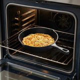 A black cast iron skillet containing a baked casserole or frittata, shown sitting on an oven rack inside an open oven.