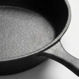 Close-up of a dark cast iron skillet showing the textured interior and part of the handle against a light gray background.