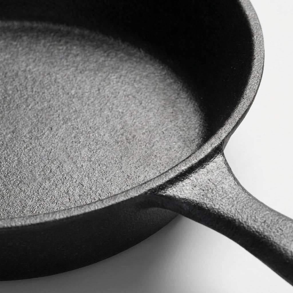 Close-up of a dark cast iron skillet showing the textured interior and part of the handle against a light gray background.