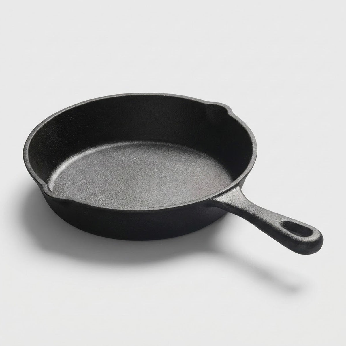 A classic black cast iron skillet with a textured interior and a loop handle, photographed on a clean light gray background.