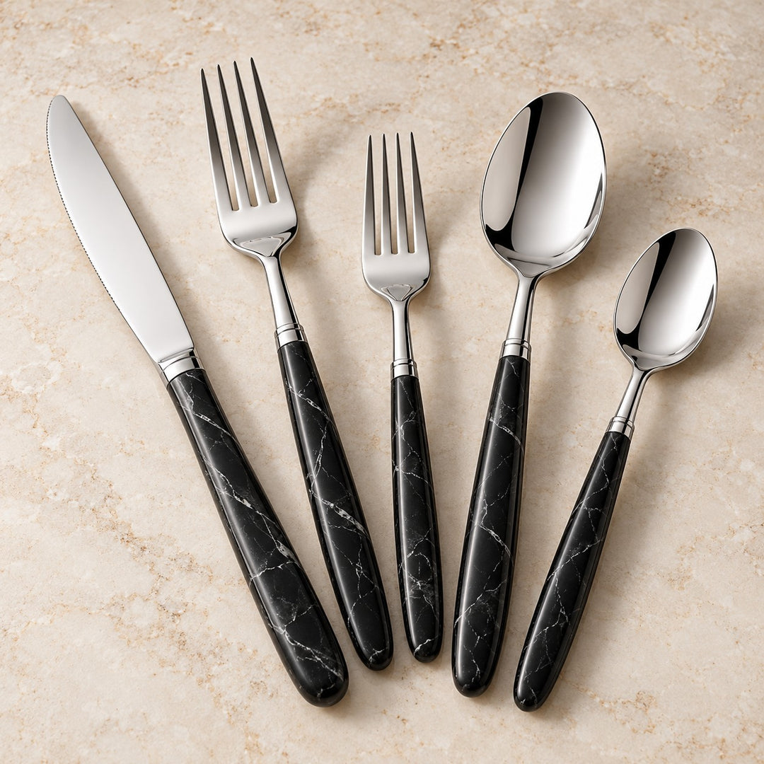 Black and silver flatware set with matching veined handles displayed together on a warm stone surface.