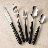 Black and silver flatware set with matching veined handles displayed together on a warm stone surface.