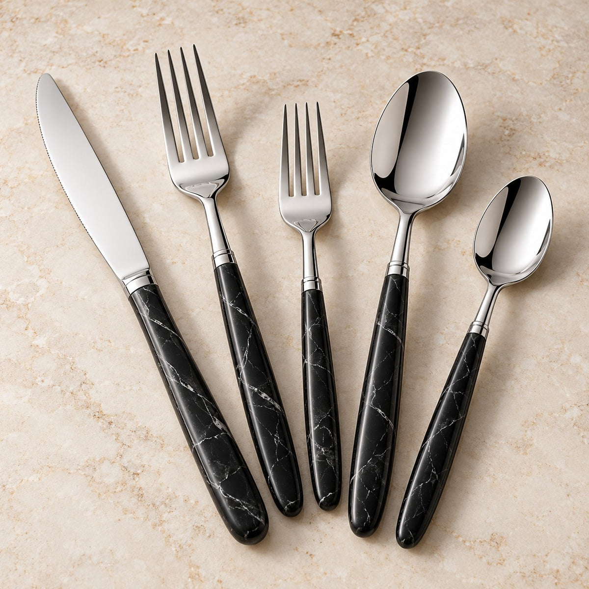 Black and silver flatware set with matching veined handles displayed together on a warm stone surface.