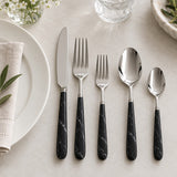 Five-piece black and silver flatware set laid beside a dinner plate to show the utensils' relative sizes.