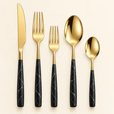 Black and gold five-piece flatware set with gold utensils and black veined handles on a light backdrop.