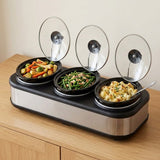 A three-compartment electric slow cooker with glass lids, shown on a wooden table with food dishes inside.