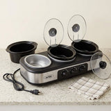 A countertop multi-pan slow cooker set with three black ceramic pots, two clear glass lids, a stainless steel insert pot, a power cord, and a folded checkered cloth on a speckled stone surface against a light beige wall.