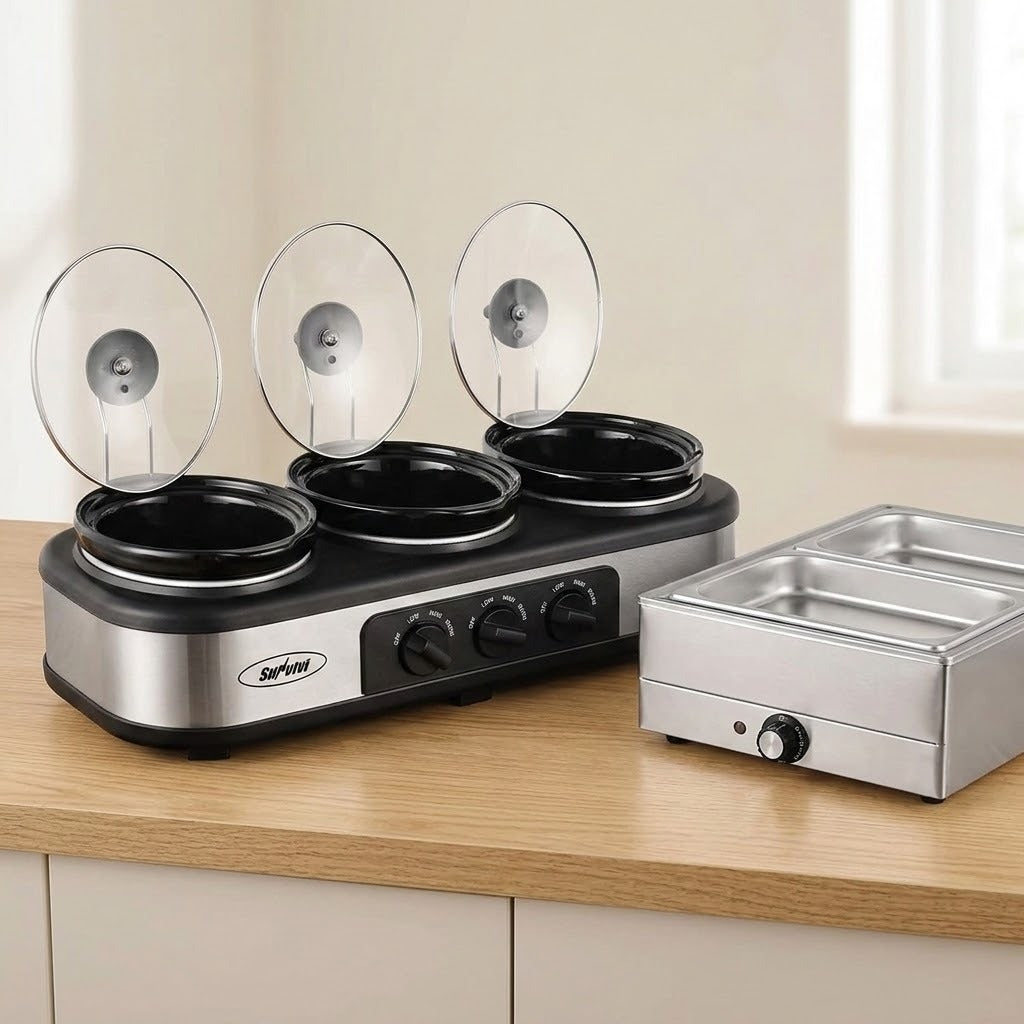 A three-compartment electric slow cooker with clear glass lids sits on a wooden countertop next to a stainless steel double compartment warmer, set against a kitchen background.