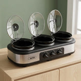 A three-slice slow cooker countertop with three glass lids propped open, set on a light wood cabinet against a sage green wall. The brand name 'Serwin' is visible on the front.