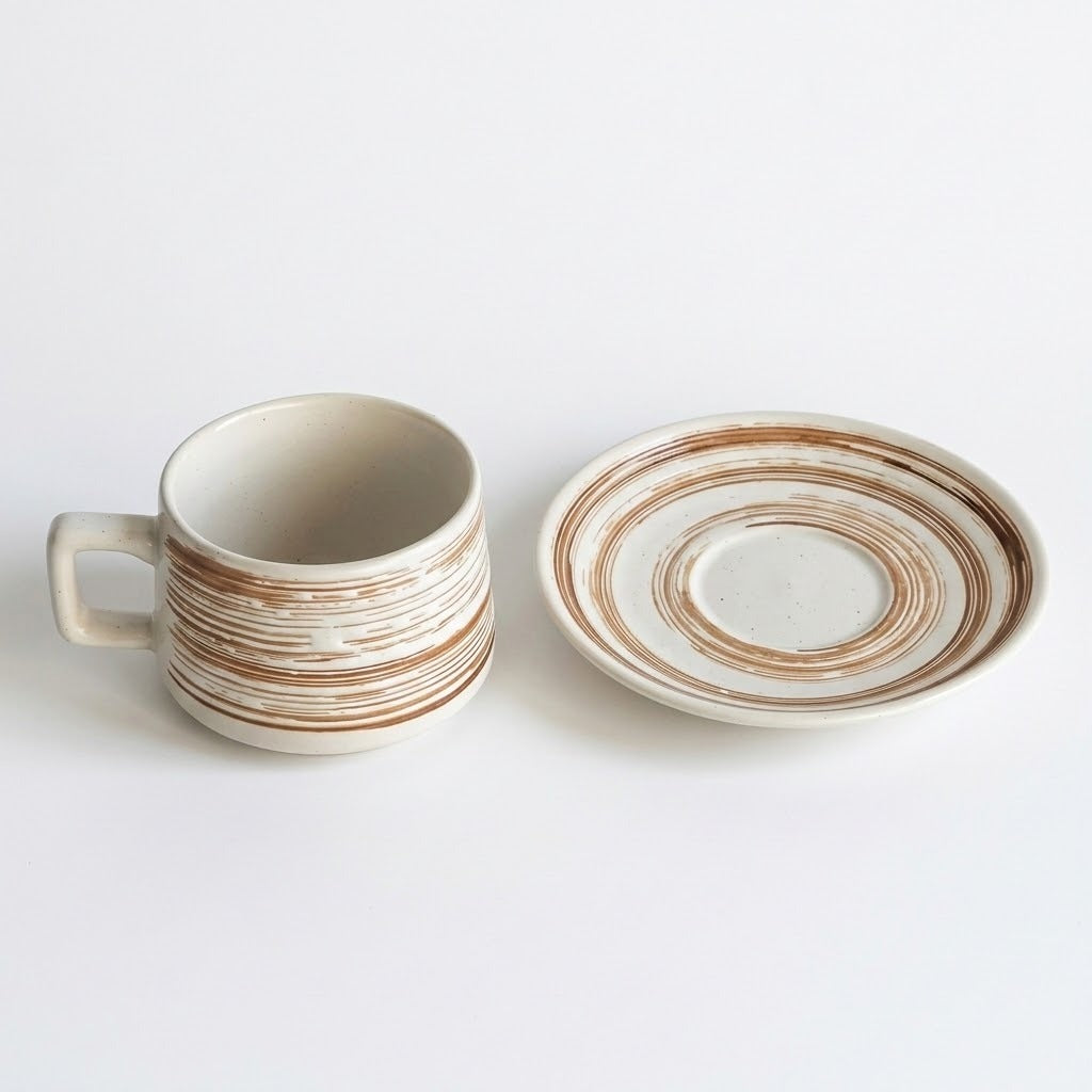 A ceramic cup with a matching saucer, both featuring a distressed cream-white glaze with hand-painted brown concentric rings, set against a plain white background.