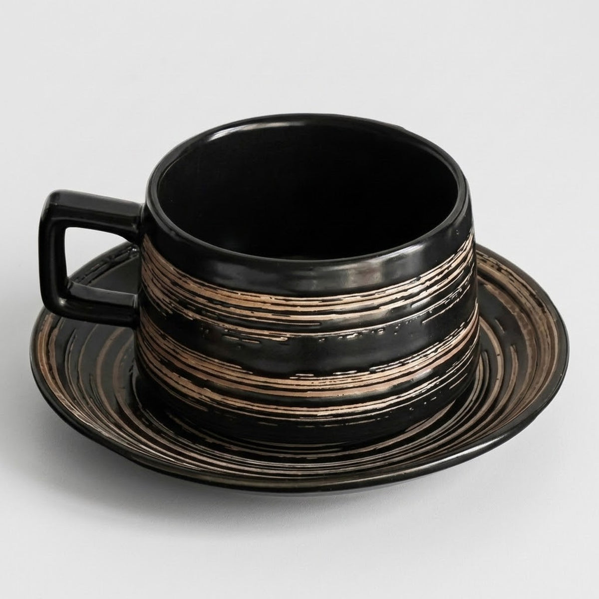 A black ceramic cup with a matching saucer, featuring horizontal distressed metallic gold and bronze stripes, set against a light gray background.